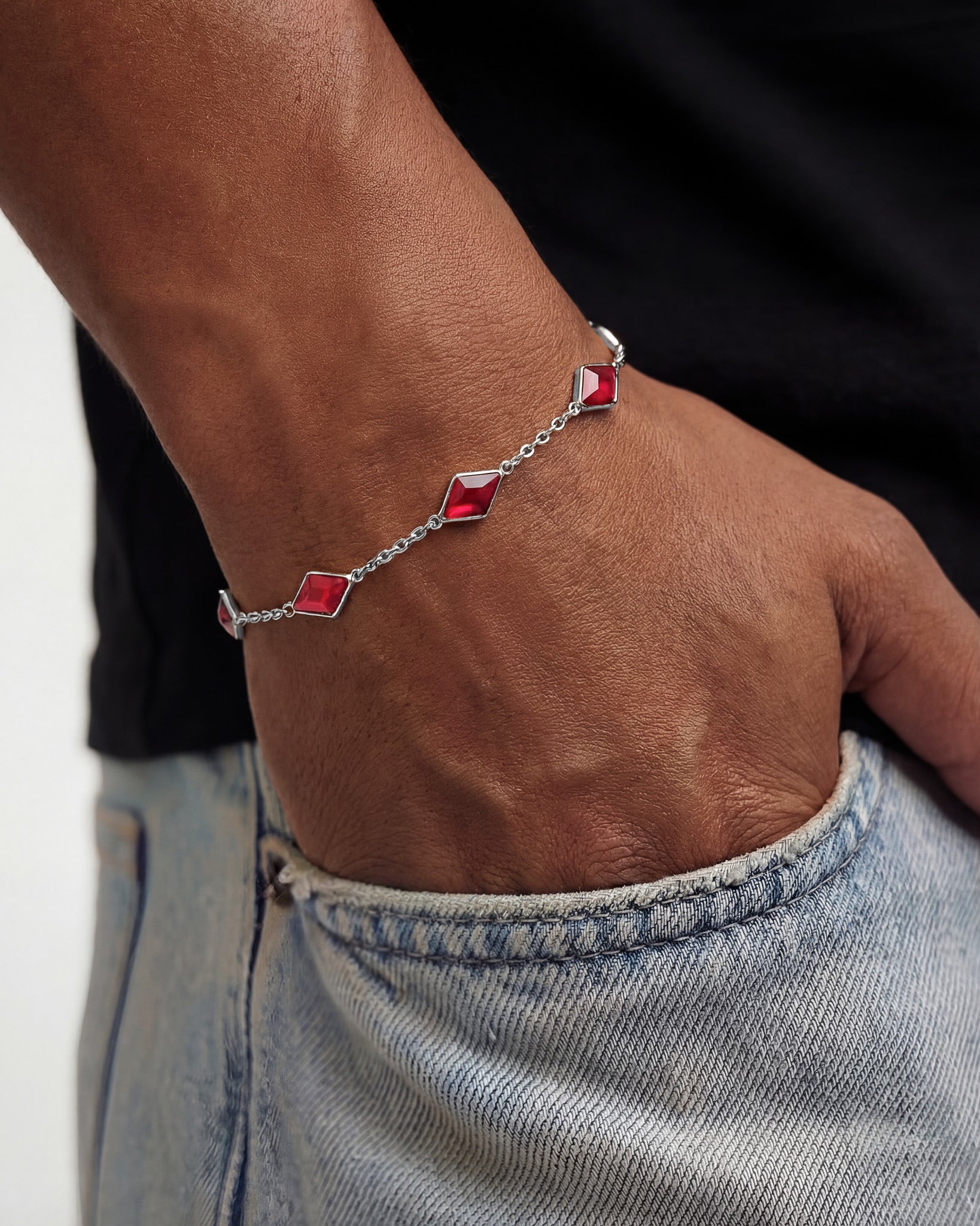 Amberes silver bracelet with red square gemstones worn on the wrist over denim fabric