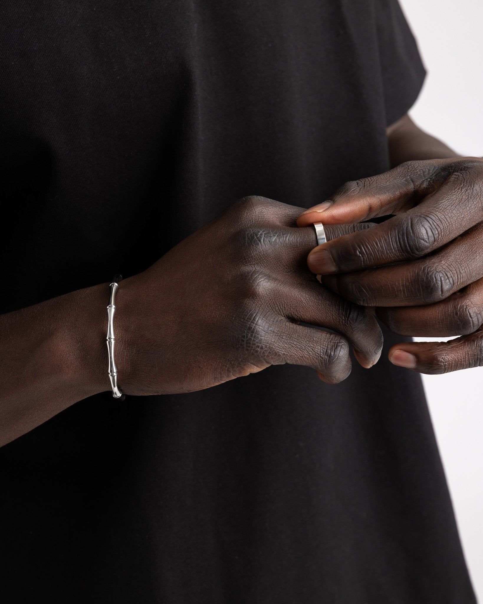 Bamboo silver bracelet worn on a dark forearm against a black fabric background