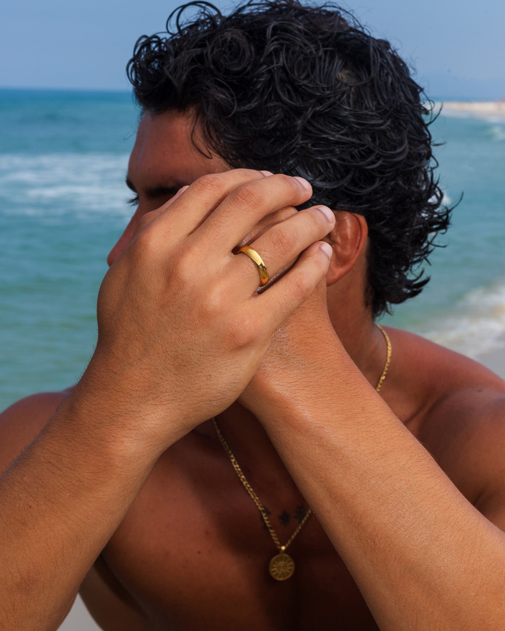 Gold band ring worn on a finger near the head with a seaside background