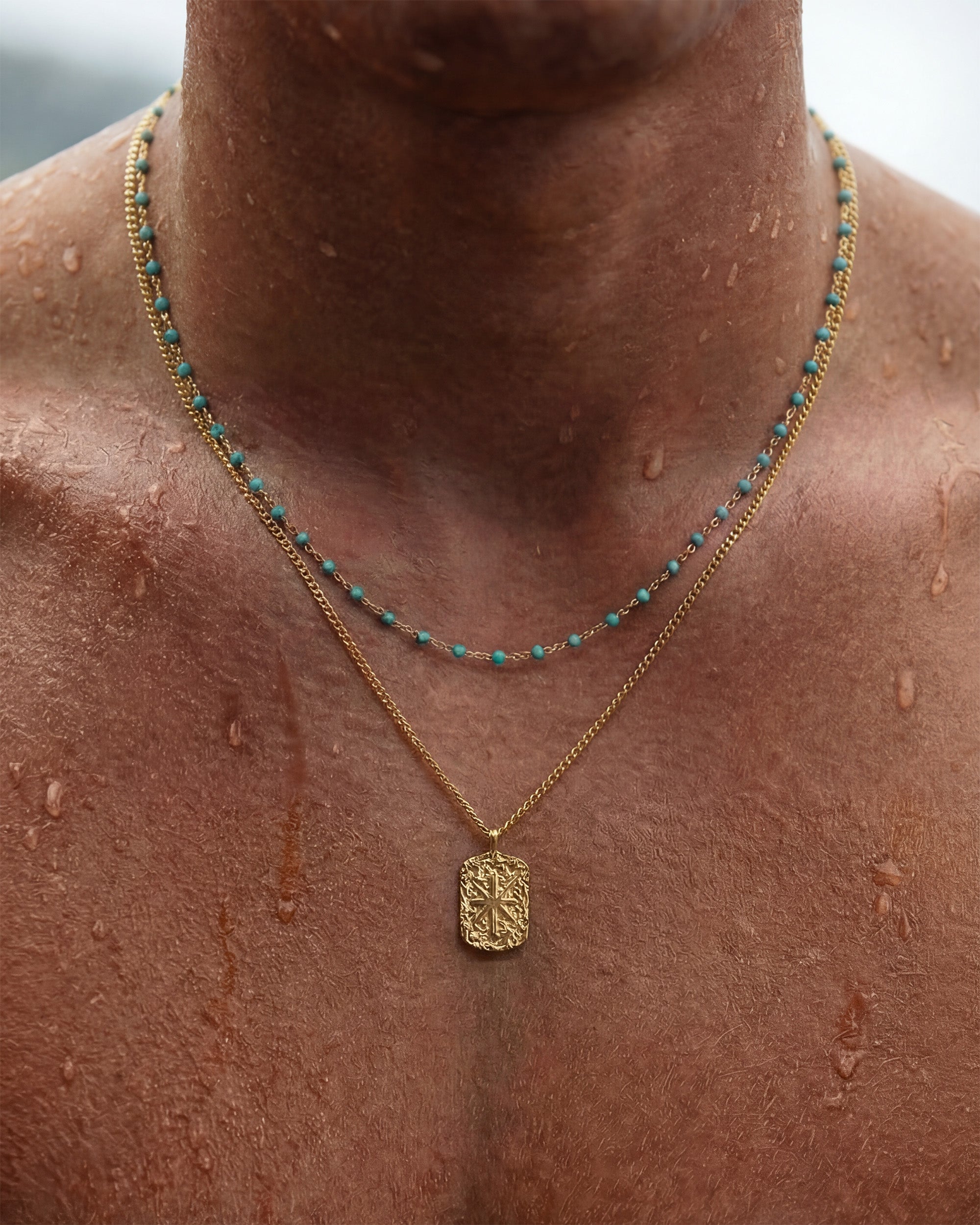 Gold chain necklace with turquoise beads and an ornate rectangular pendant resting on the chest.