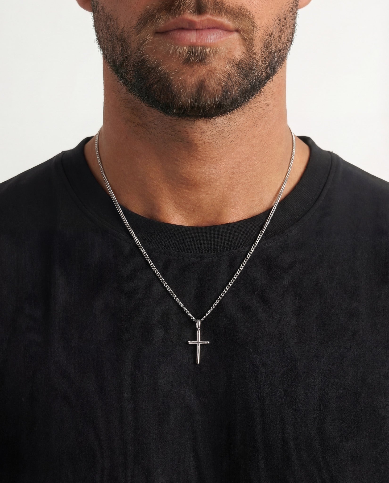 Silver cross pendant on a textured chain around a man's neck