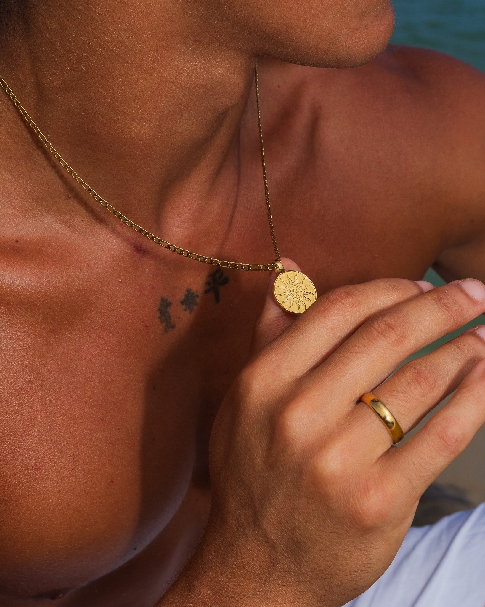 Gold energy necklace with a round sunburst pendant worn on a tanned chest.