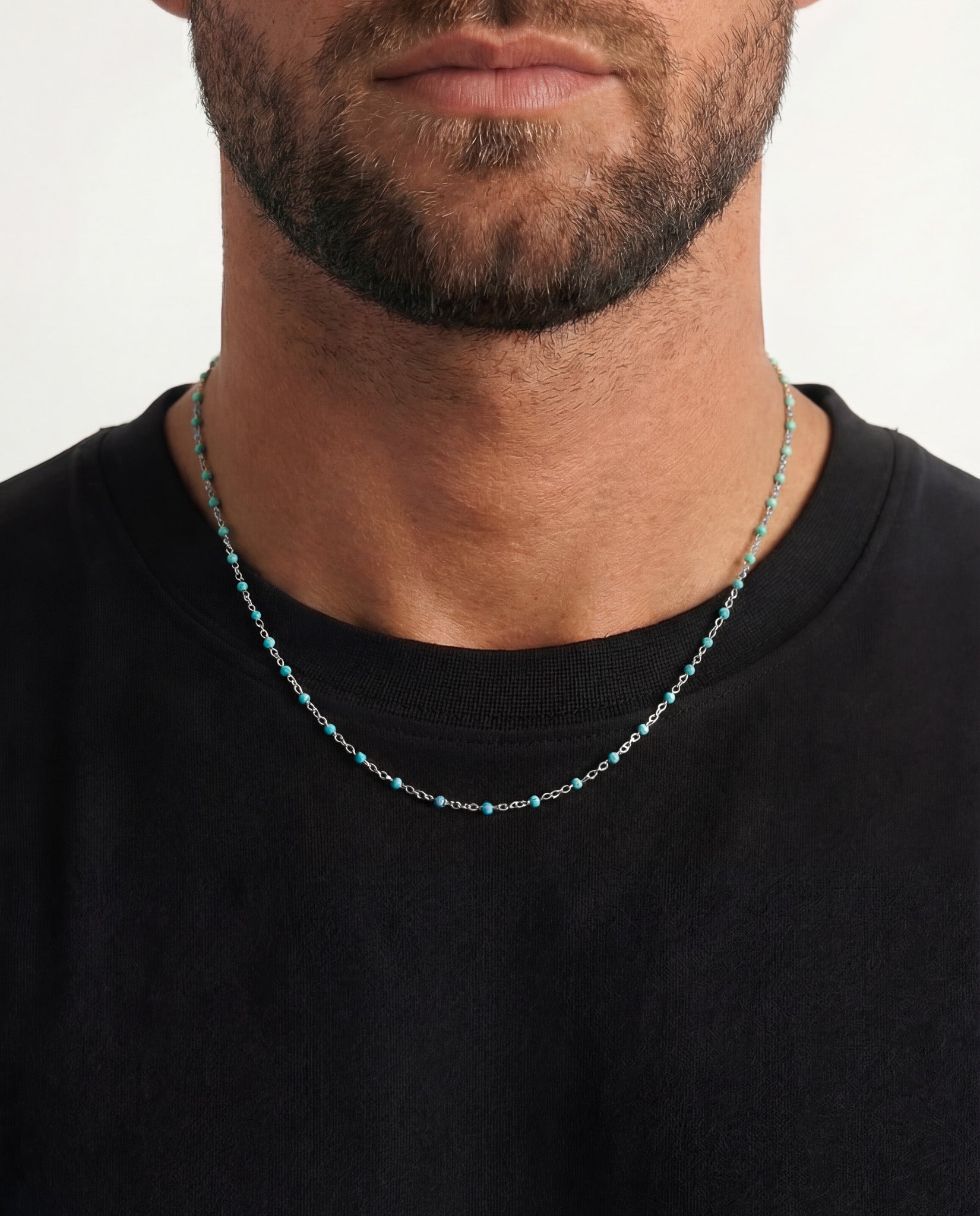 Close-up of a silver chain necklace with turquoise beads worn on a man’s neck over a black shirt