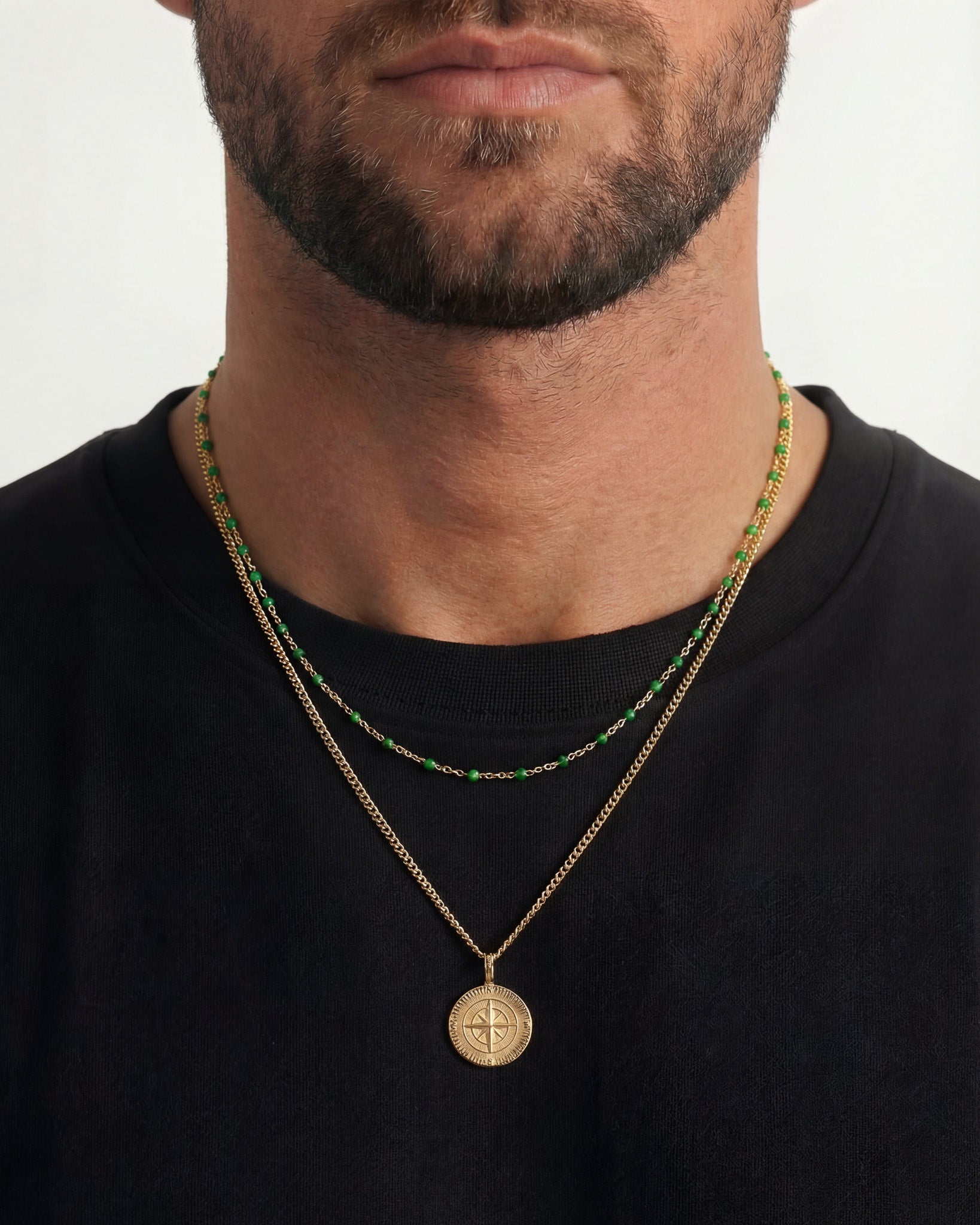 Bearded man wearing two gold chains with green beads and a round pendant