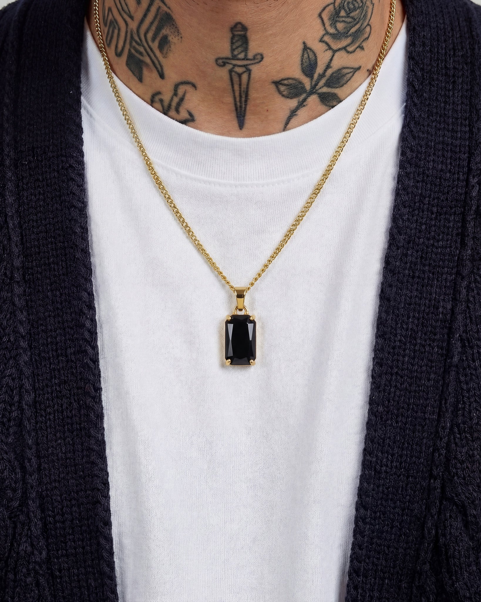 VOLT GOLD NECKLACE with a rectangular black gemstone pendant resting on a white T shirt under a dark cardigan