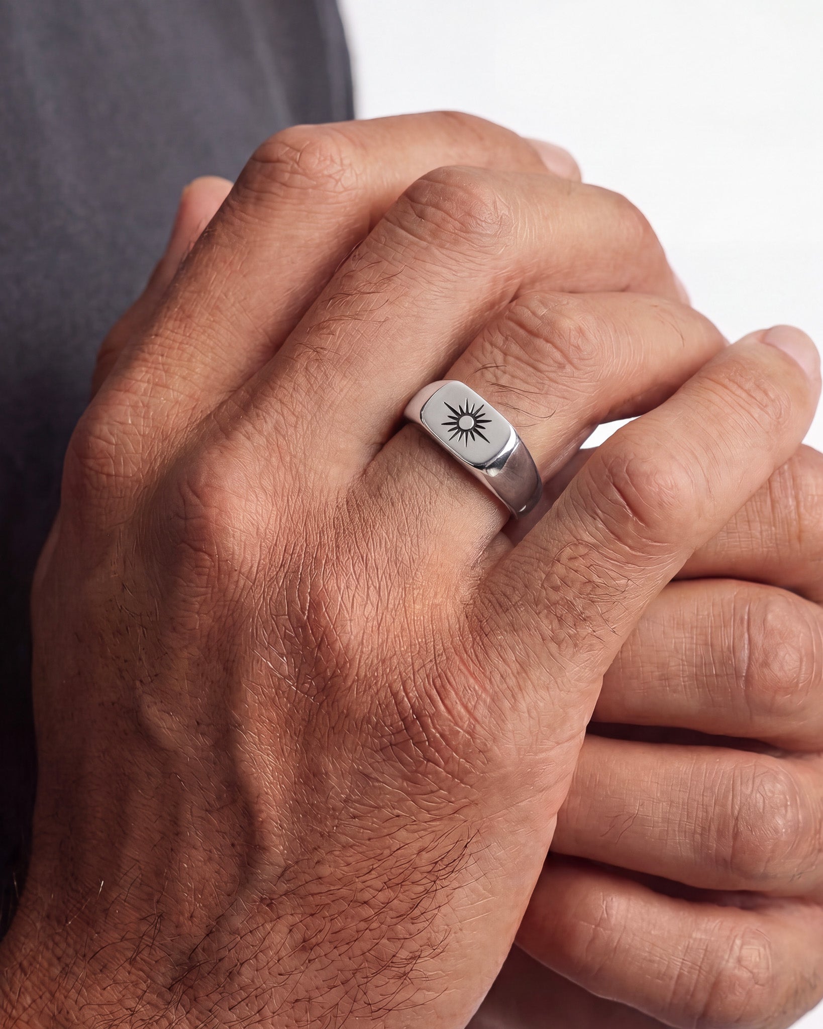 Close-up of a hand wearing a silver signet ring with a sunburst design.