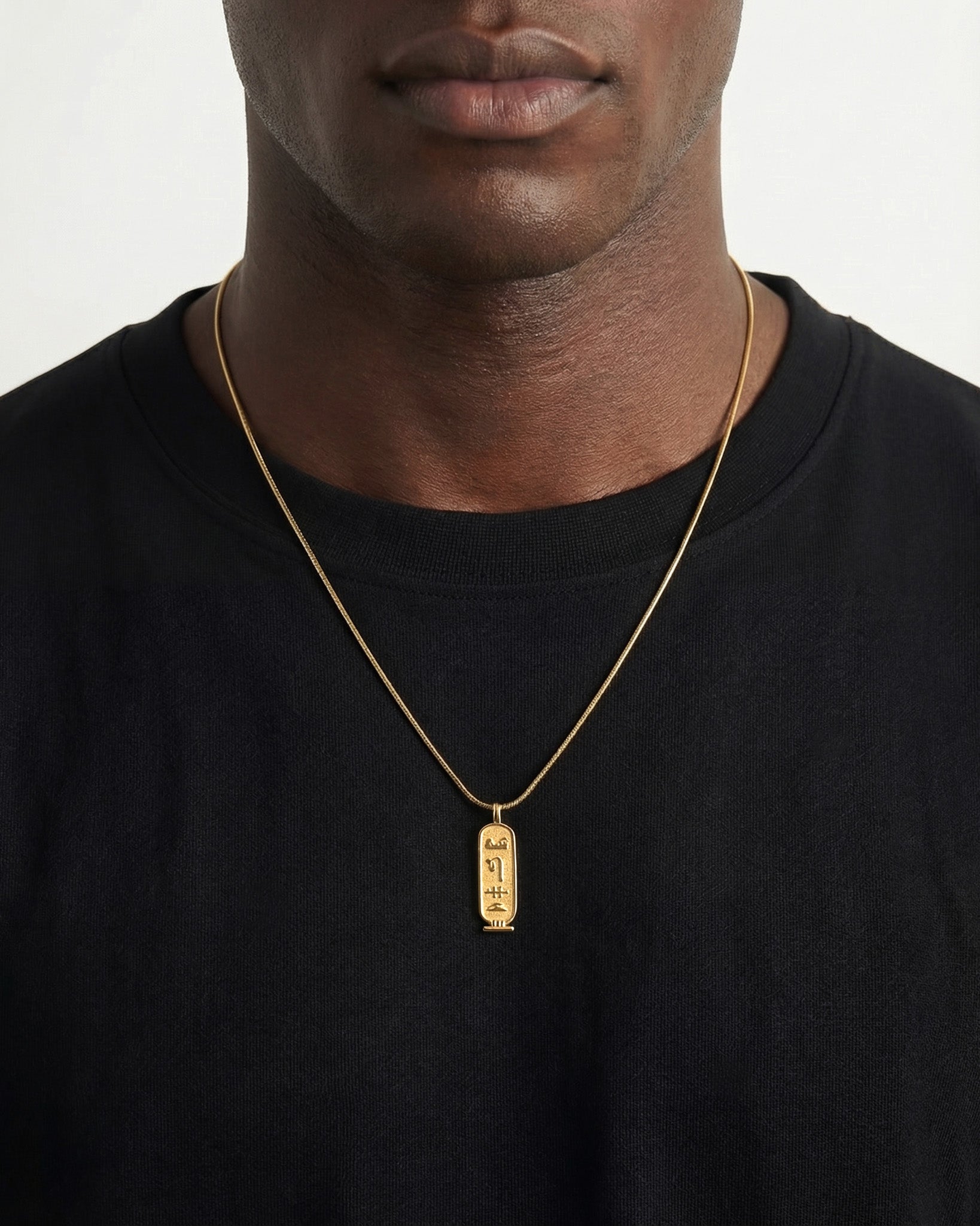 Neck shot of a man wearing the Luxor Gold Necklace with a hieroglyph engraved pendant resting on a black shirt