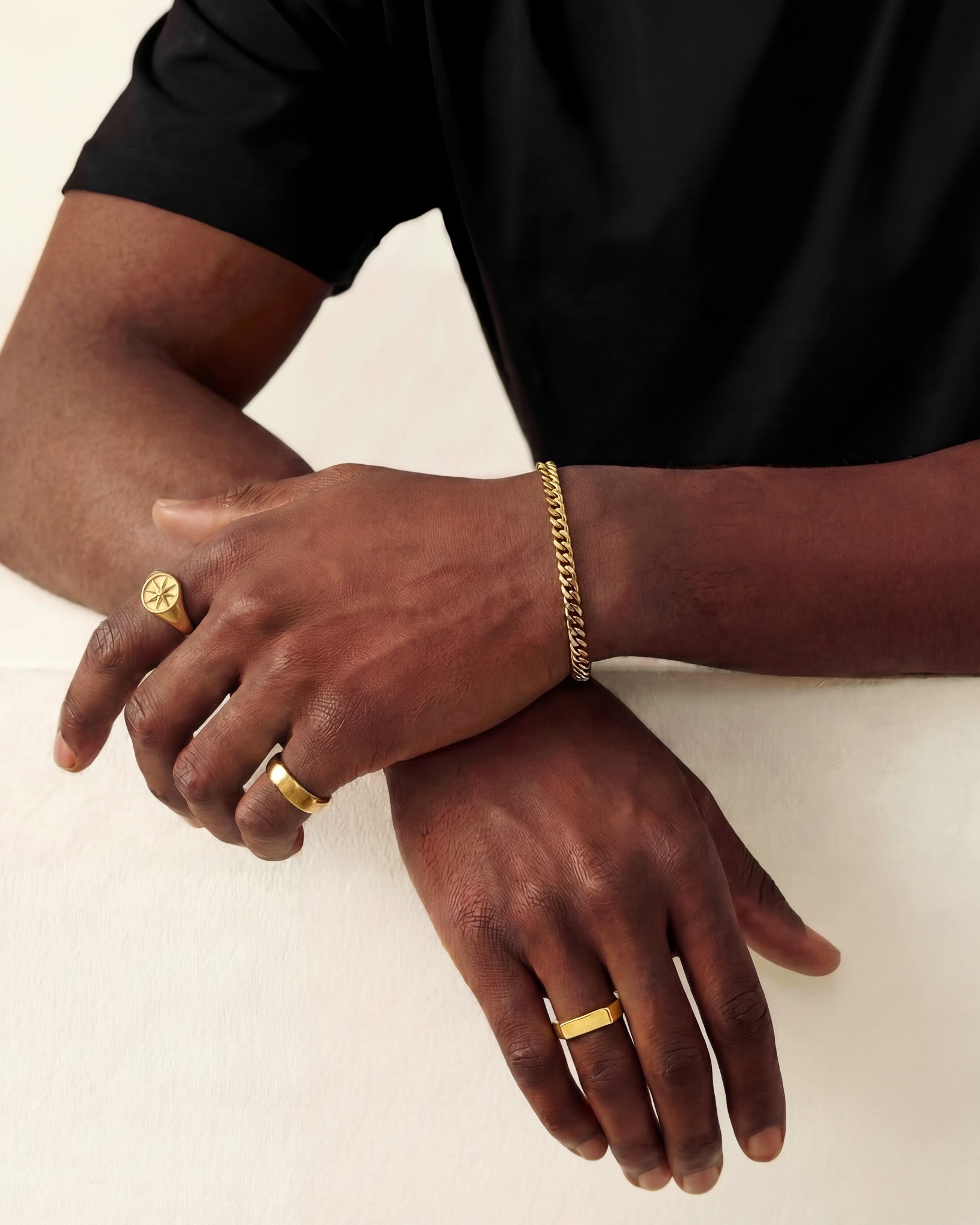 Close-up of a gold Milo ring with a round emblem on the finger, paired with a slim gold bracelet.