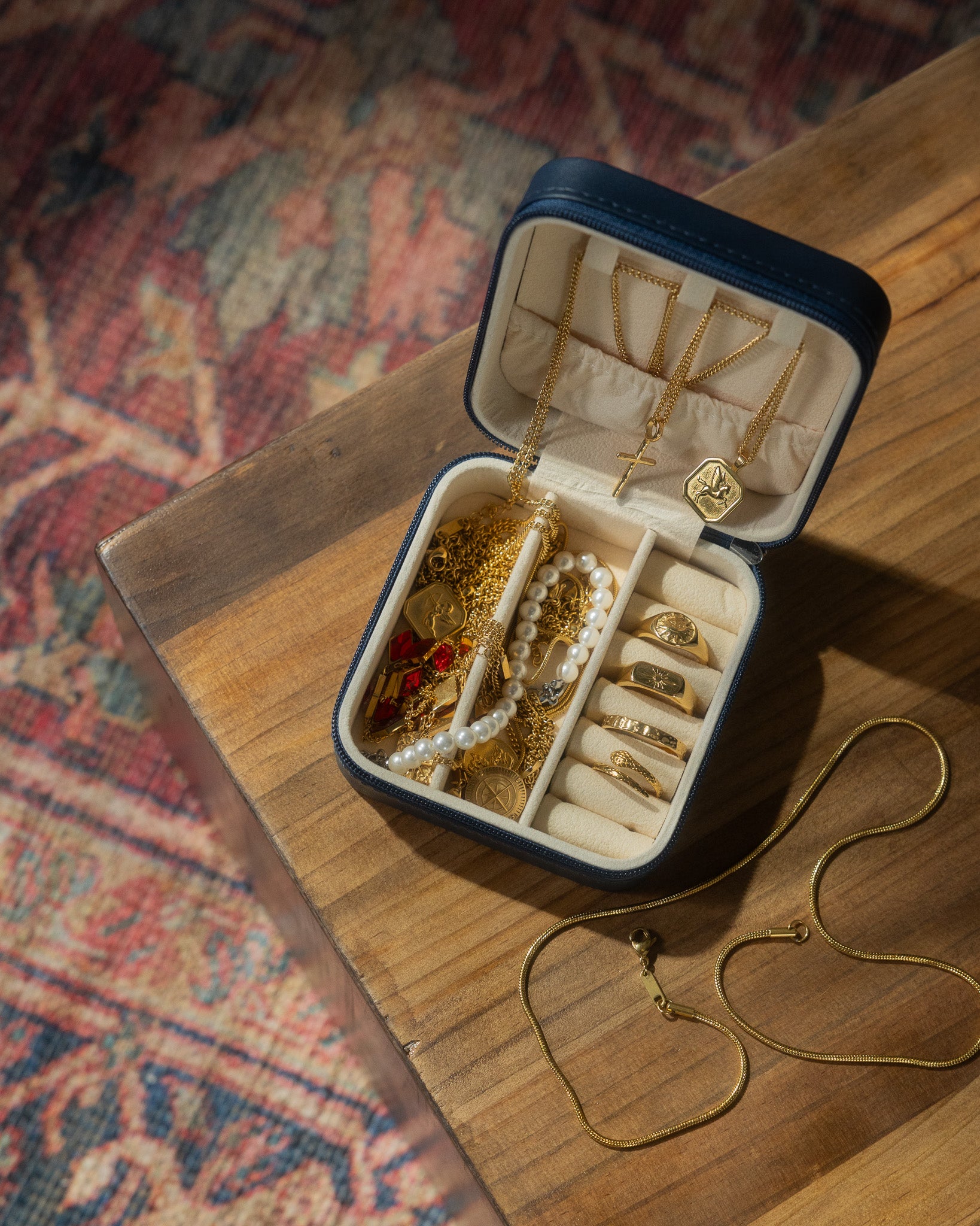 Open navy case on a wooden table filled with gold chains rings and pearl jewelry