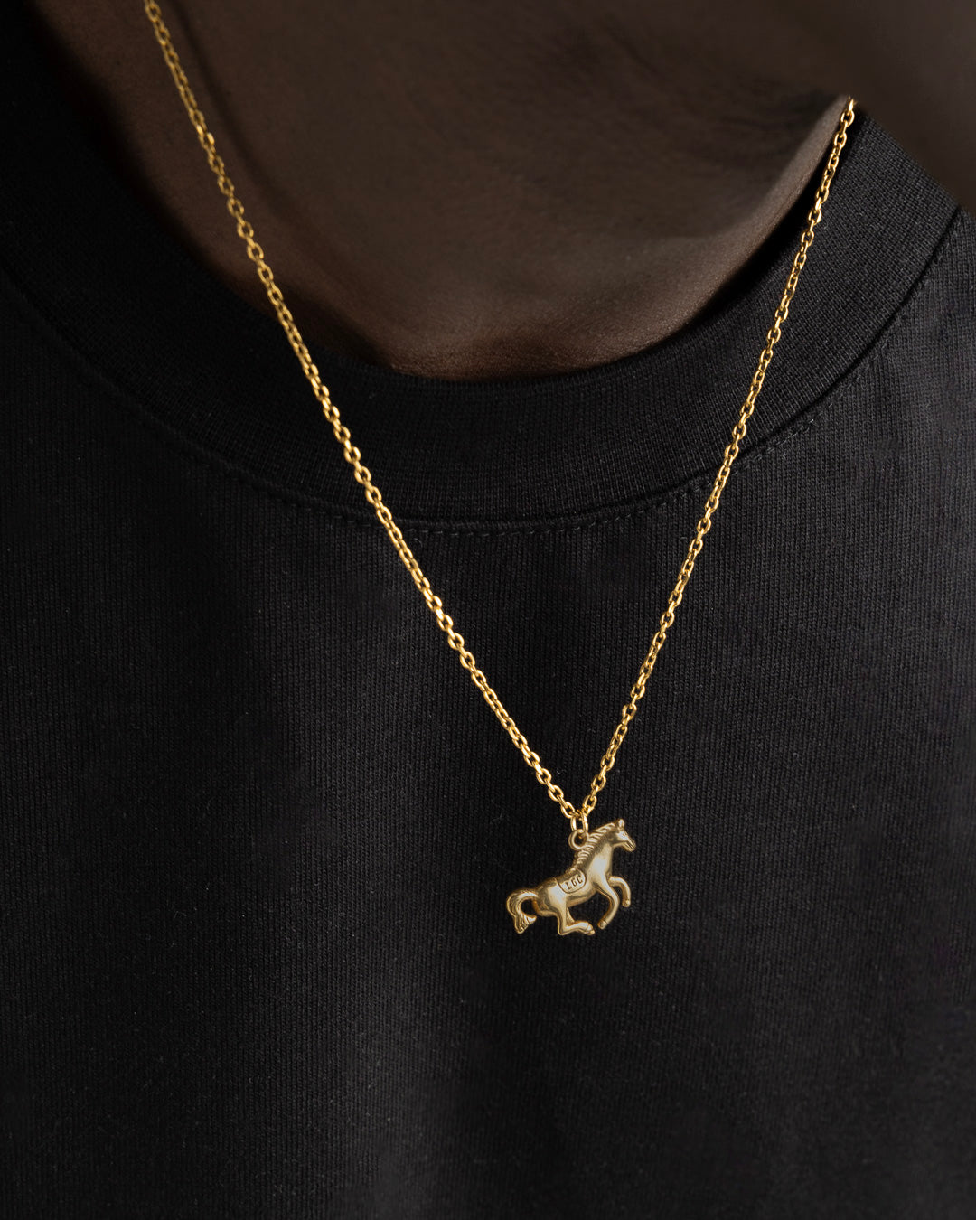 Close-up of Monaco Gold Necklace showing the horse pendant on a gold chain worn over a white tee.