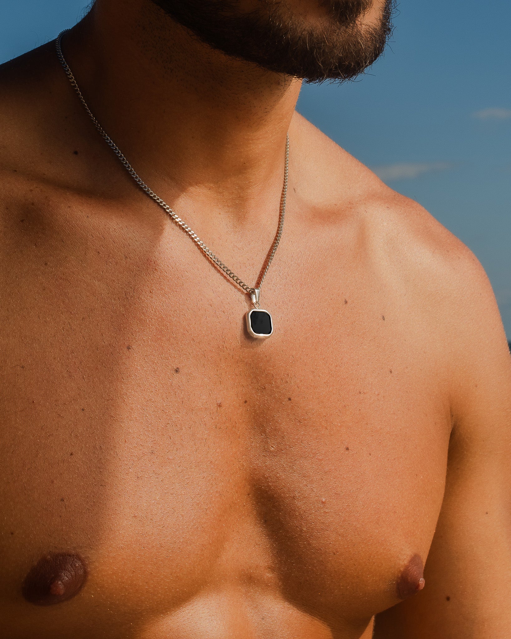 Nova Silver Necklace chain draped over a man's bare chest against a blue sky