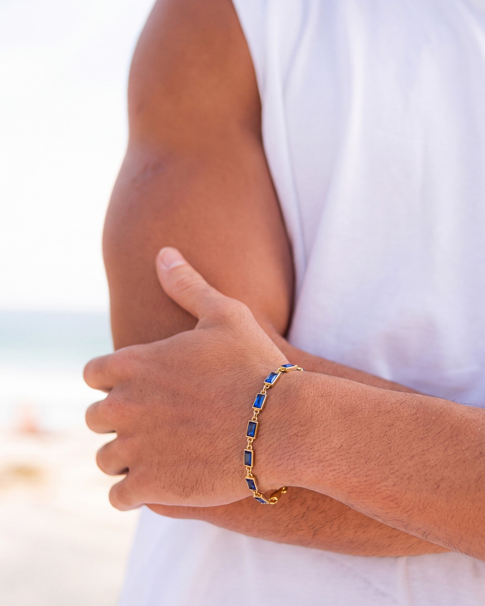 Partial view of the OMEN gold bracelet with blue stones on an arm near a white shirt.