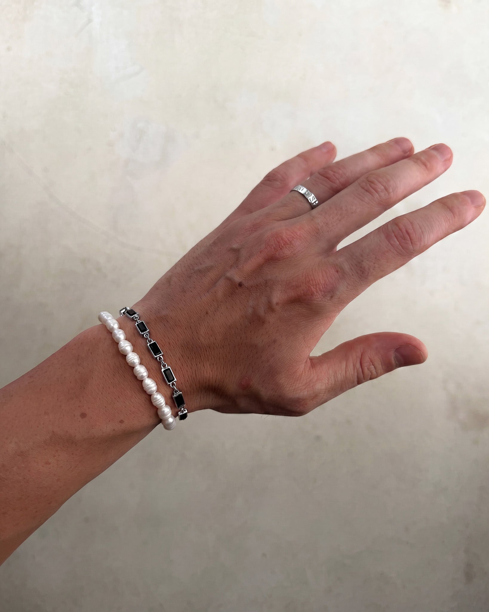 Silver OMEN bracelet with square black stone links along the wrist.
