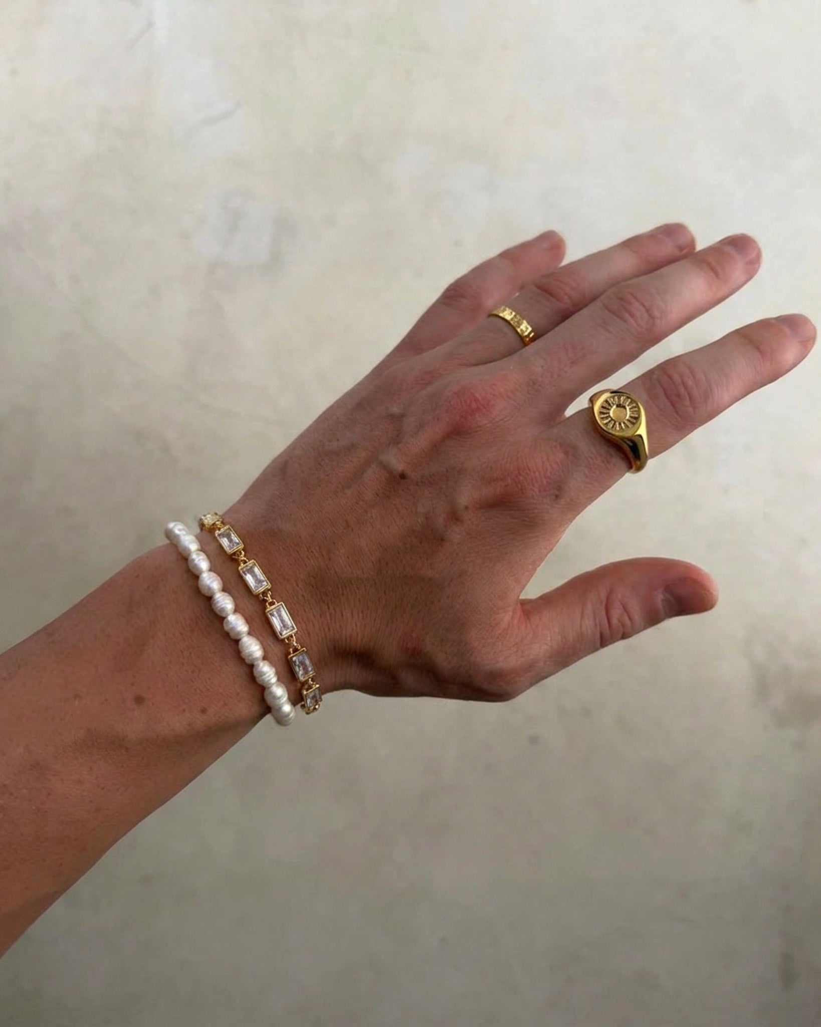 Gold OMEN bracelet with square textured links on the wearer's wrist.