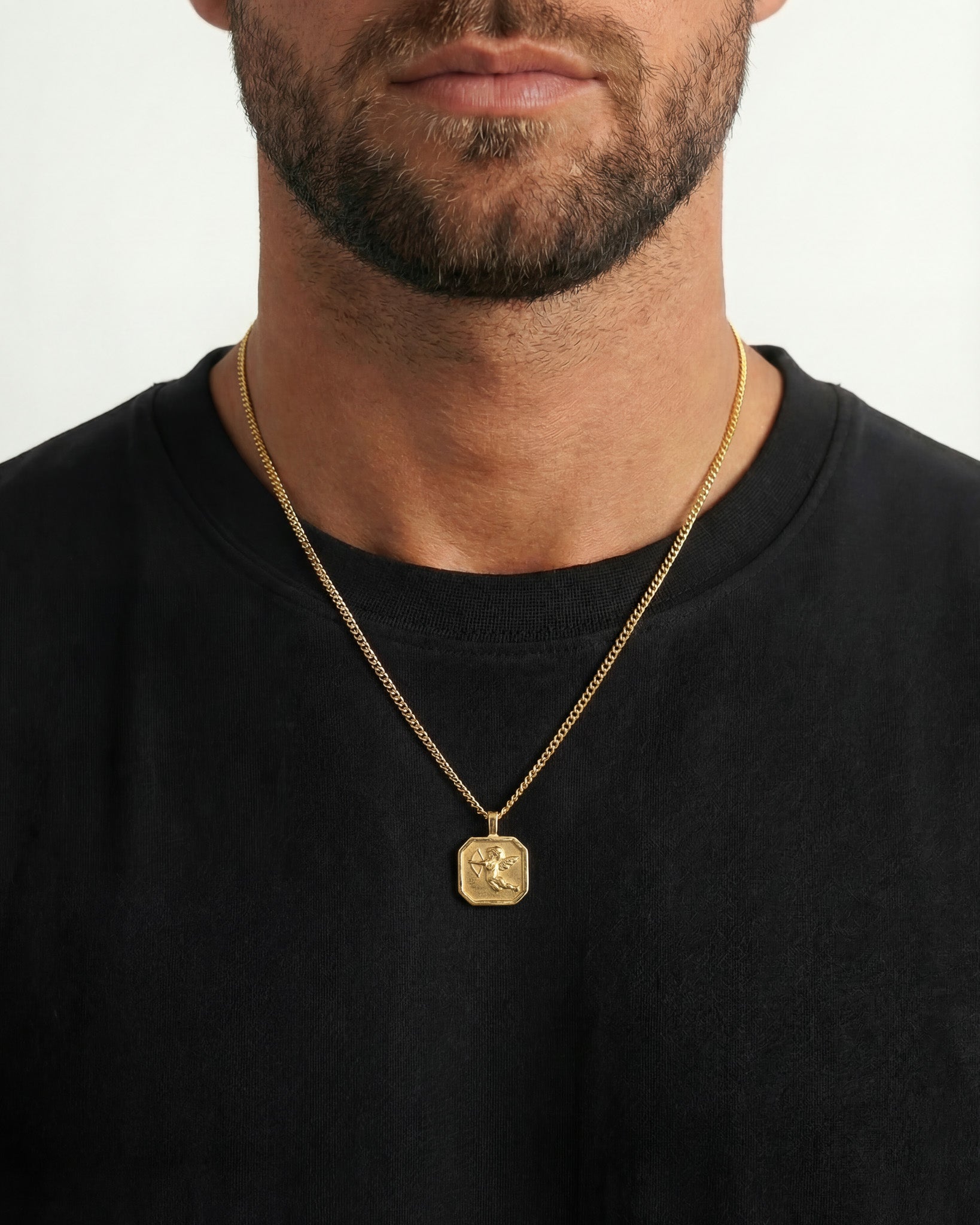 Close up of a gold chain necklace with Cupid pendant resting on a black shirt