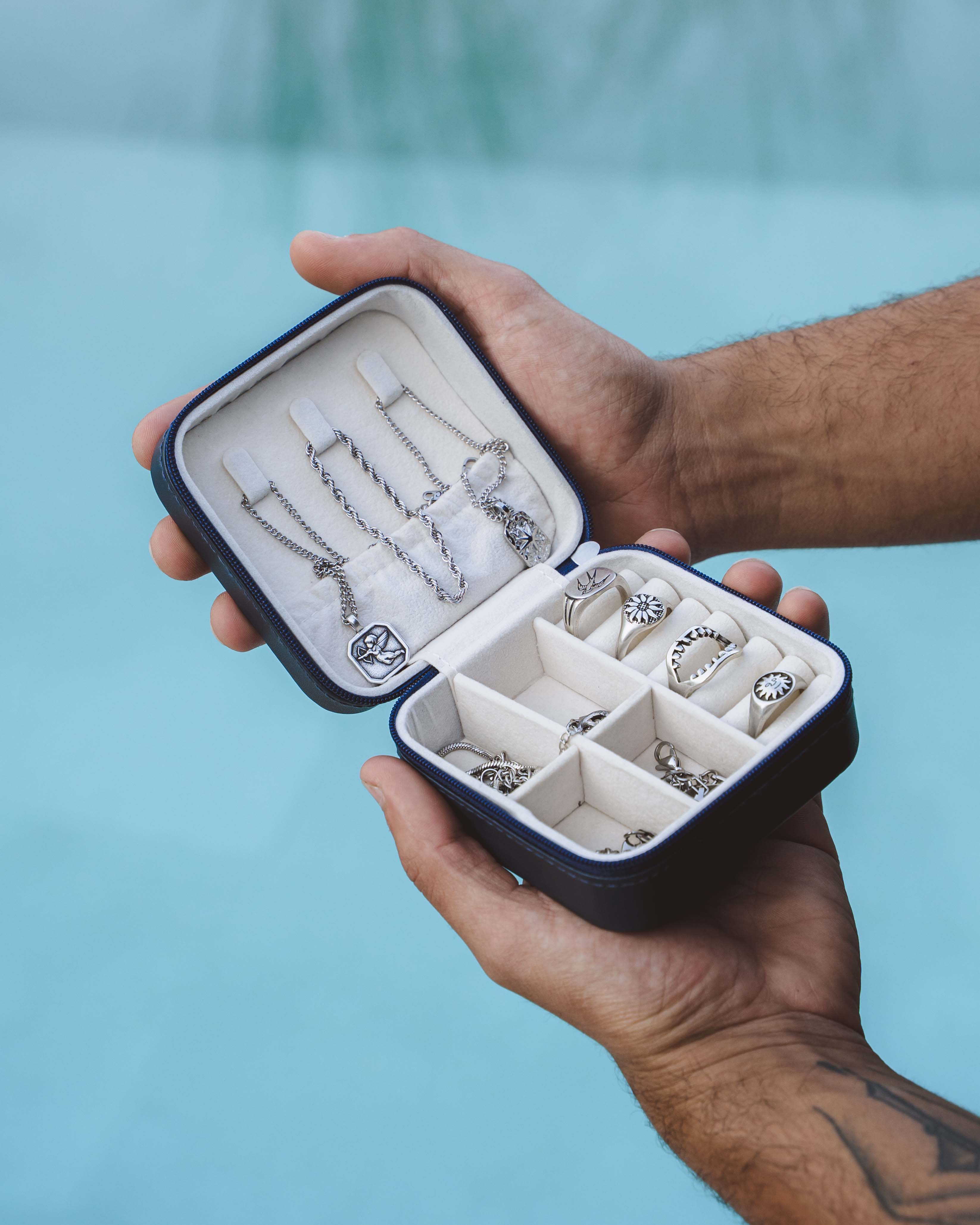 Open navy travel jewelry case displaying silver chains and rings on a light interior