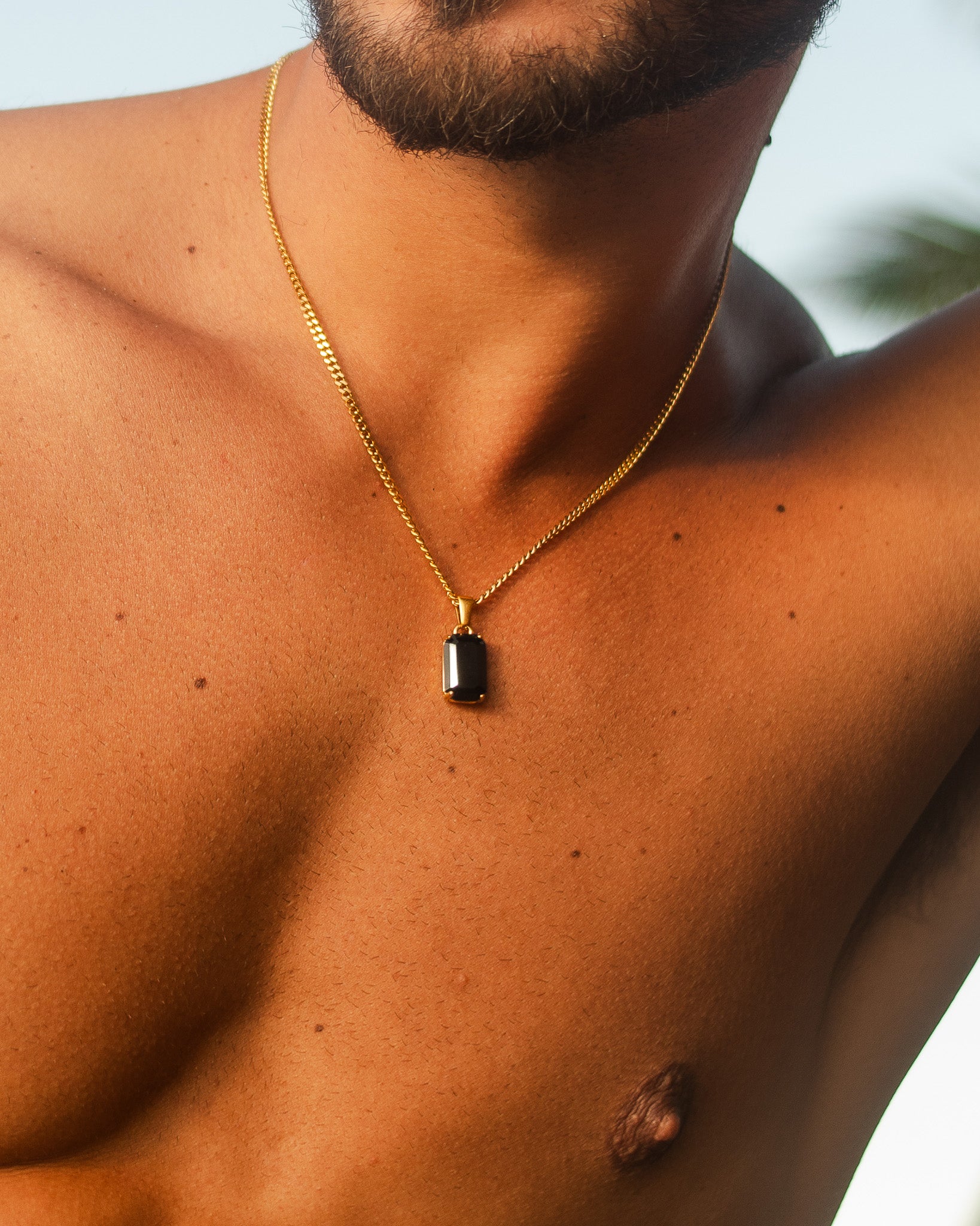 VOLT gold necklace with a small dark rectangular pendant resting on the chest.