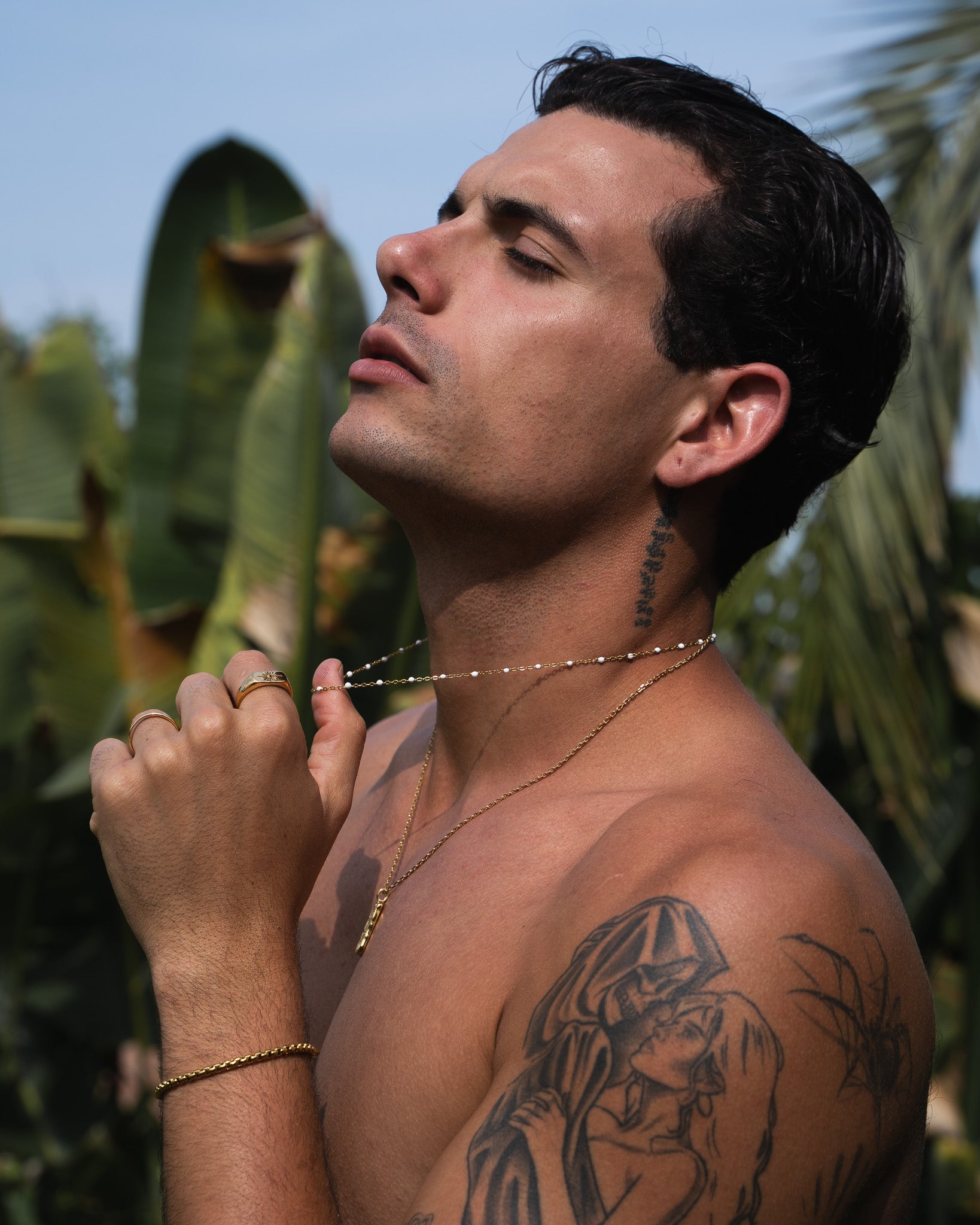 Man wearing layered GEM GOLD CHAIN with white bead accents outdoors against a bright backdrop